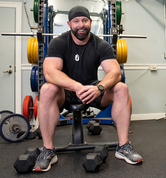 male Veteran in black shirt and shorts sitting on a bench   
press at the gym 